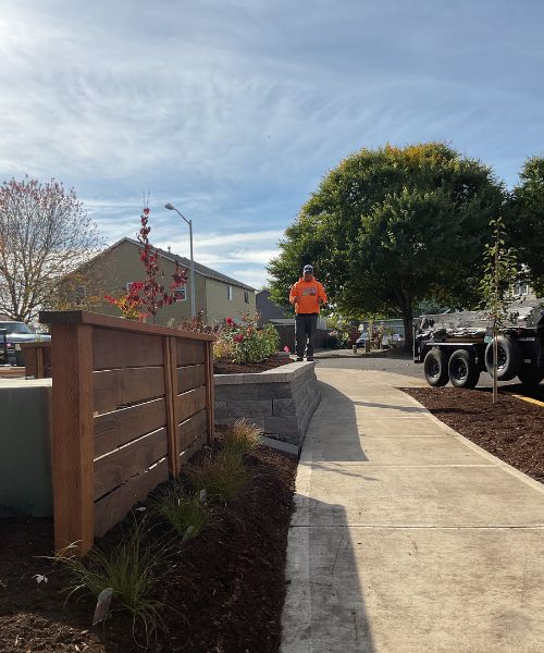 A man walking down a sidewalk next to a wooden fence